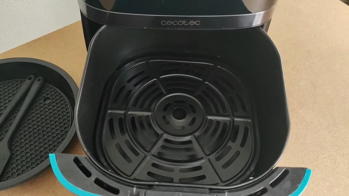 Cuve du Cecotec Cecofry 5500 Pro avec son double fond perforé, à côté du tapis et de la spatule en silicone fournis