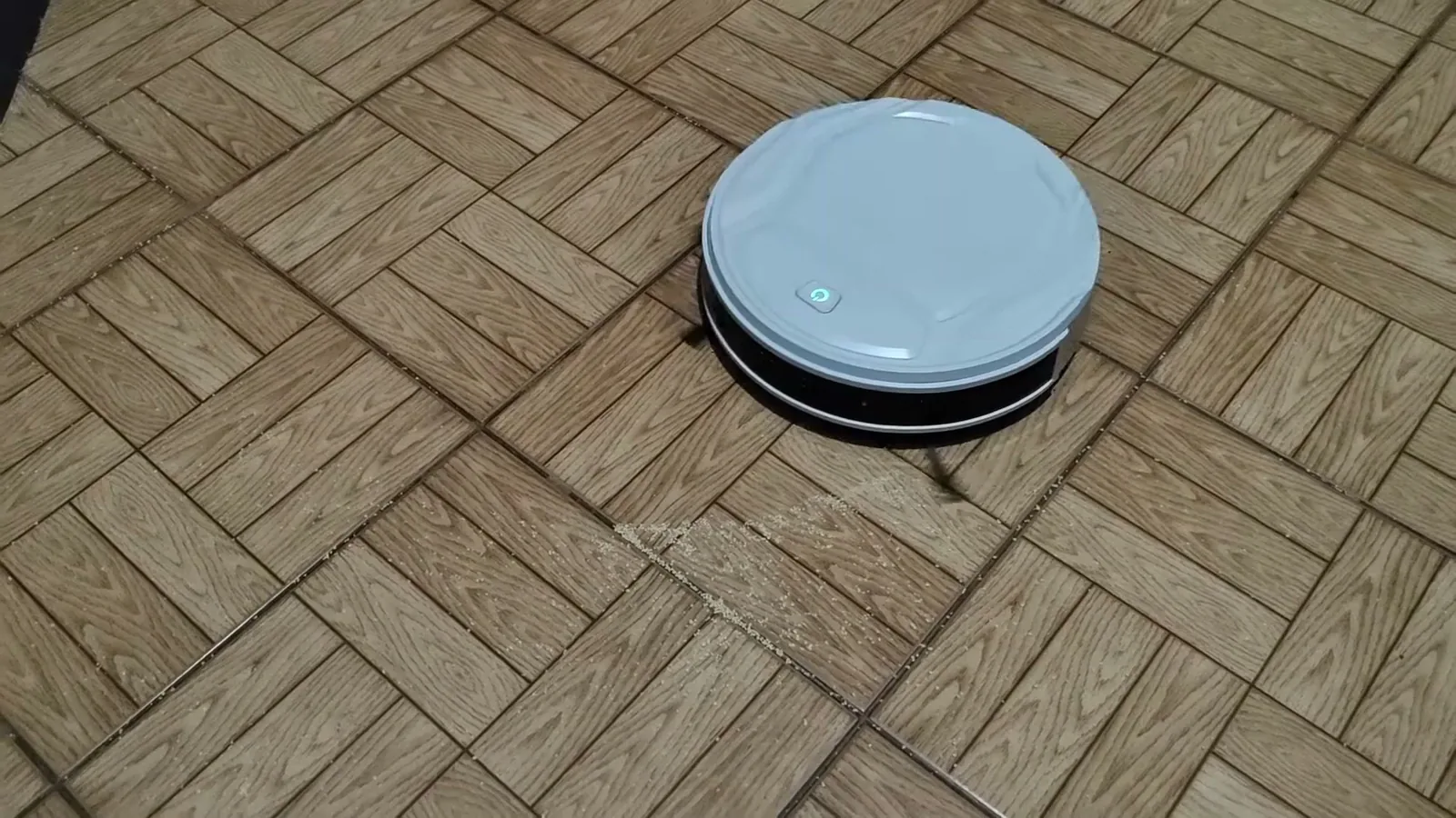 Le robot aspirateur Lefant M210P en action sur un sol imitation parquet parsemé de semoule
