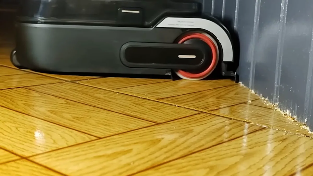 Le bras robotisé du Mova M50 Ultra déployé contre une plinthe pour ramener les débris du bord du mur